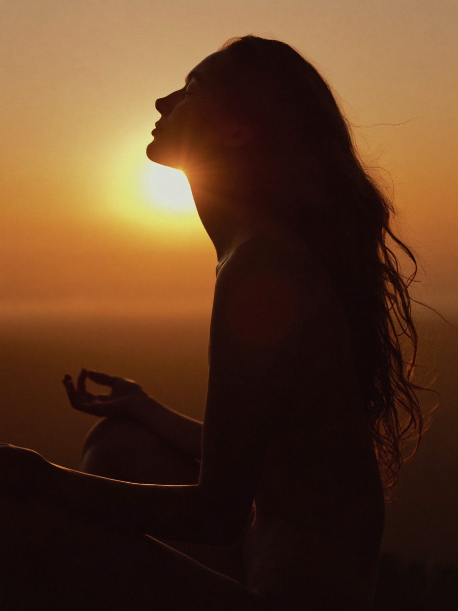 A woman breathing deeply at sunrise, calm and centered